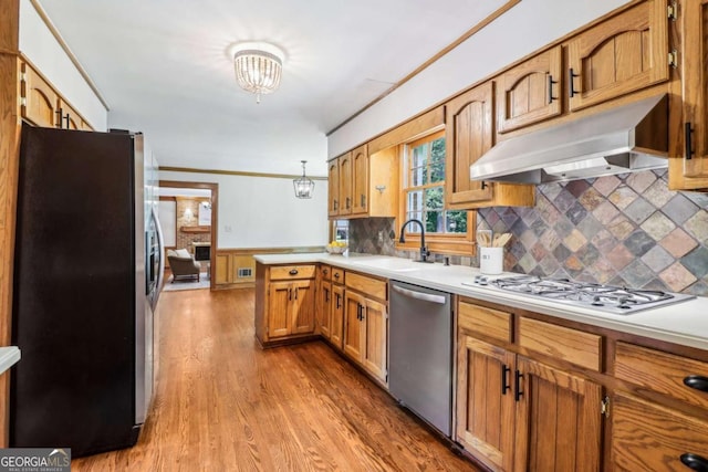 kitchen featuring stainless steel appliances, under cabinet range hood, a sink, a peninsula, and light countertops