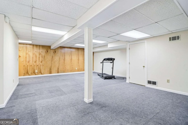 finished below grade area with a paneled ceiling, carpet floors, wood walls, and baseboards