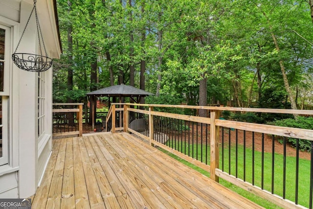 deck featuring a gazebo, view of wooded area, and a yard