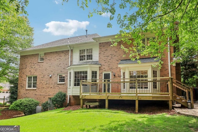 rear view of property featuring a yard, a deck, and brick siding