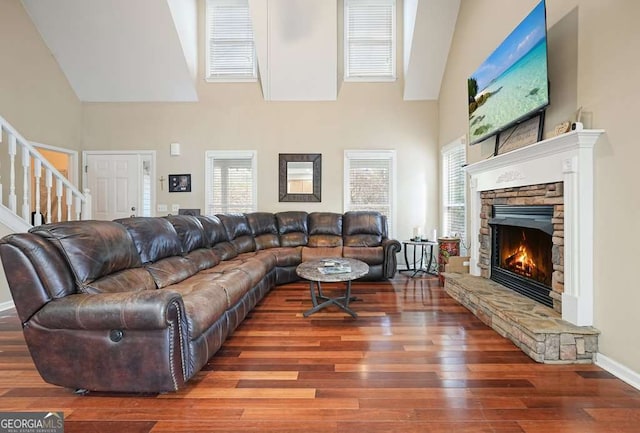 living room featuring a towering ceiling, wood finished floors, stairs, a fireplace, and baseboards