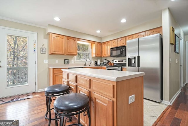 kitchen featuring appliances with stainless steel finishes, a center island, a sink, light countertops, and ornamental molding