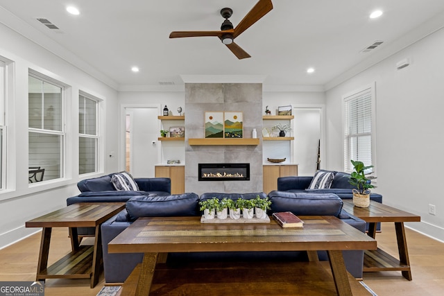 living area with ceiling fan, light wood finished floors, a fireplace, crown molding, and baseboards