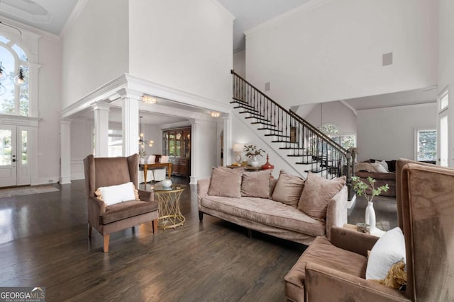 living area with a towering ceiling, ornamental molding, stairway, wood finished floors, and ornate columns