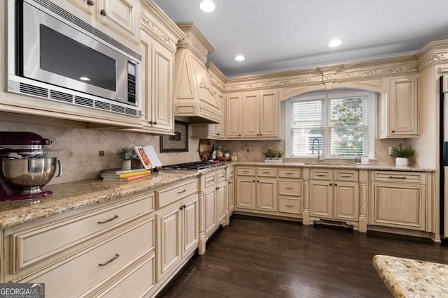 kitchen with appliances with stainless steel finishes, cream cabinetry, dark wood-type flooring, backsplash, and recessed lighting