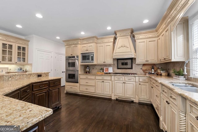 kitchen with cream cabinetry, stainless steel appliances, a sink, ornamental molding, and light stone counters