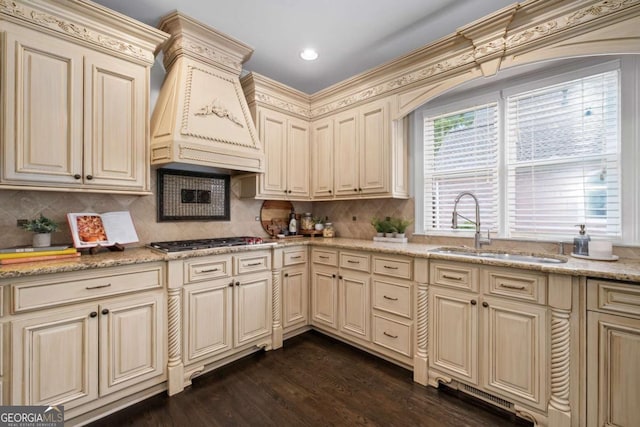 kitchen featuring cream cabinets, a sink, custom exhaust hood, stainless steel gas stovetop, and backsplash