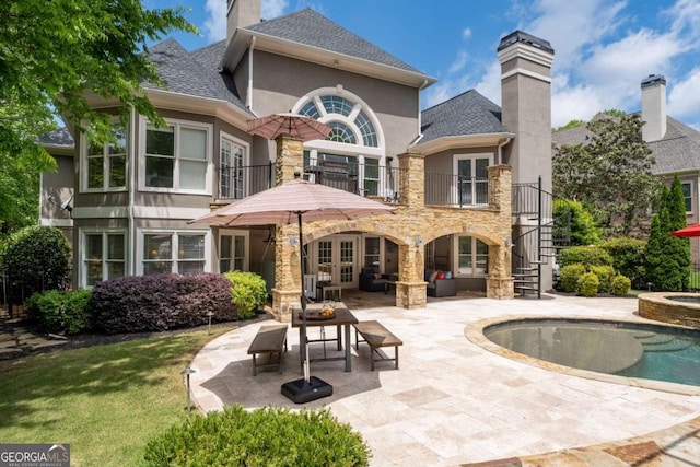 rear view of house featuring a balcony, a chimney, stucco siding, a patio, and french doors