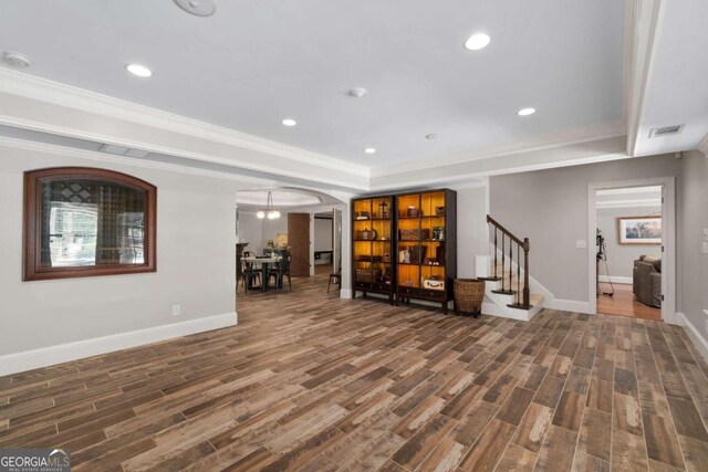 living area with wood finished floors, a tray ceiling, baseboards, arched walkways, and stairs