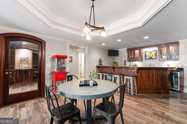 dining area with wine cooler, crown molding, wood finished floors, bar with sink, and a tray ceiling