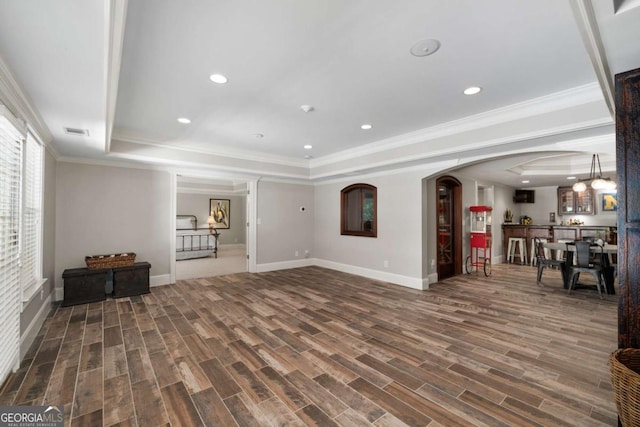 unfurnished living room with a raised ceiling, baseboards, wood finished floors, crown molding, and recessed lighting
