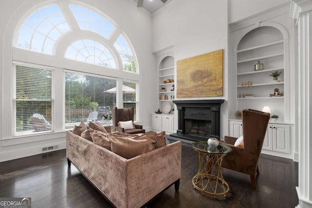 living room with built in shelves, dark wood finished floors, a high ceiling, a fireplace with raised hearth, and baseboards
