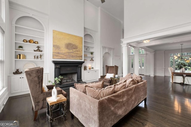 living room featuring built in features, a fireplace, dark wood-style floors, crown molding, and a decorative wall