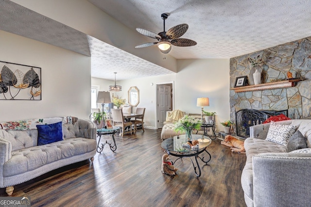living room featuring a textured ceiling, a ceiling fan, wood finished floors, a stone fireplace, and baseboards