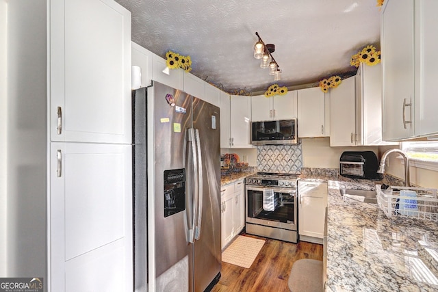 kitchen featuring appliances with stainless steel finishes, a sink, wood finished floors, light stone counters, and white cabinetry