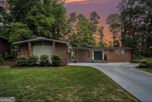 view of front of house featuring brick siding, a yard, concrete driveway, and a chimney
