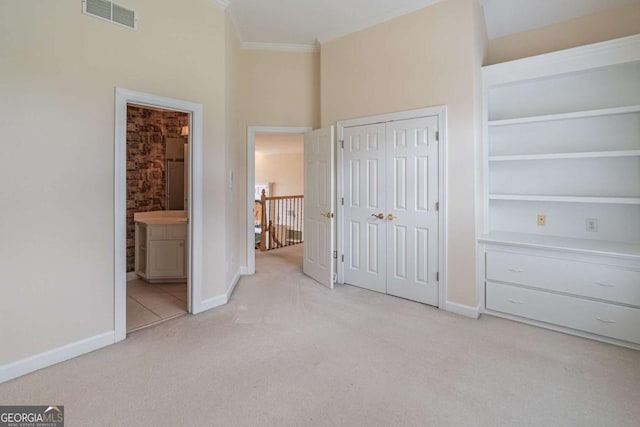 unfurnished bedroom featuring light carpet, baseboards, crown molding, a closet, and ensuite bath