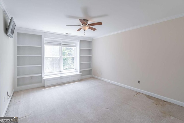 carpeted empty room featuring crown molding, ceiling fan, built in shelves, and baseboards