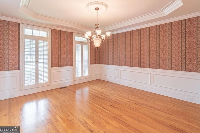 spare room featuring wainscoting, a chandelier, wallpapered walls, ornamental molding, and wood finished floors