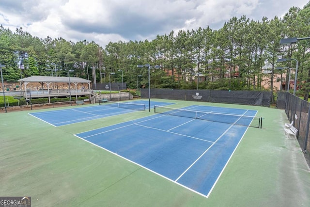 view of tennis court featuring fence, community basketball court, and view of wooded area