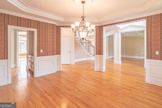 unfurnished dining area featuring a chandelier, ornamental molding, a wainscoted wall, stairway, and wallpapered walls
