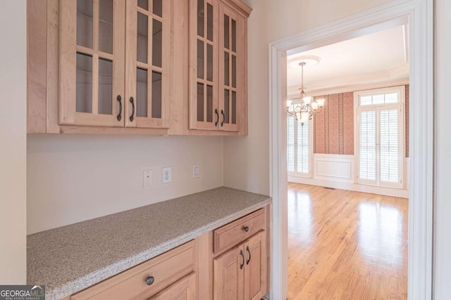 kitchen featuring ornamental molding, light wood-style floors, glass insert cabinets, a chandelier, and light brown cabinets