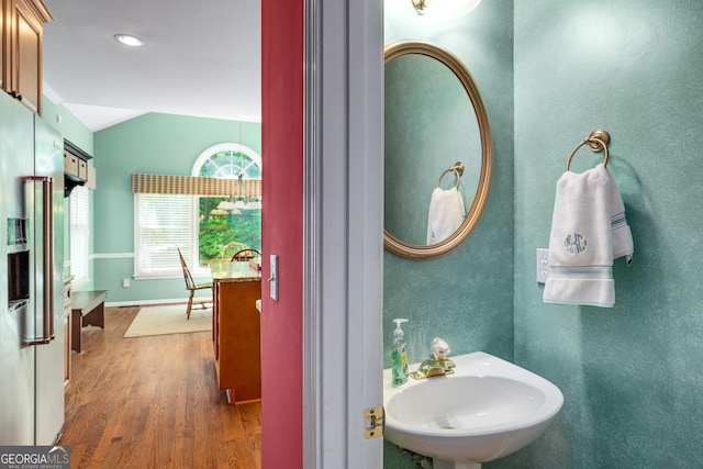 bathroom featuring vaulted ceiling, wood finished floors, a sink, and baseboards