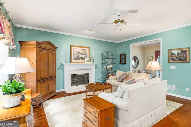 living area featuring wood finished floors, crown molding, ceiling fan, a glass covered fireplace, and baseboards