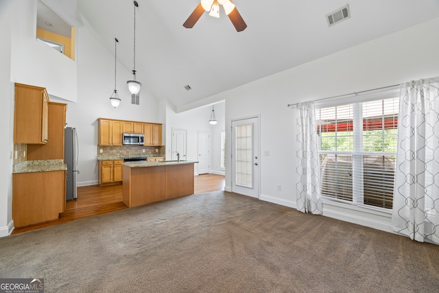 924 Vinings Dr, Winder, GA 30680 - kitchen featuring appliances with stainless steel finishes, high vaulted ceiling, dark carpet, ceiling fan, and a center island with sink