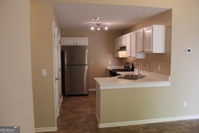 kitchen featuring stainless steel appliances, stone finish floors, under cabinet range hood, a sink, and white cabinetry