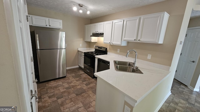kitchen featuring freestanding refrigerator, a sink, gas range oven, under cabinet range hood, and stone finish floors