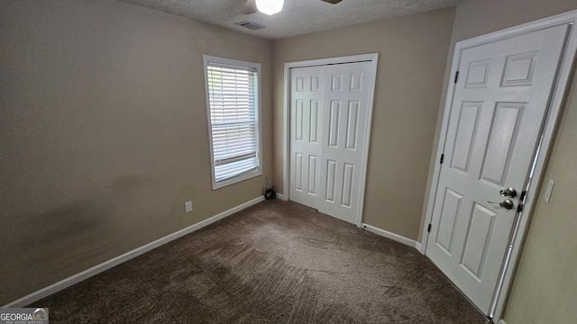 unfurnished bedroom with dark colored carpet, baseboards, a closet, multiple windows, and a textured ceiling