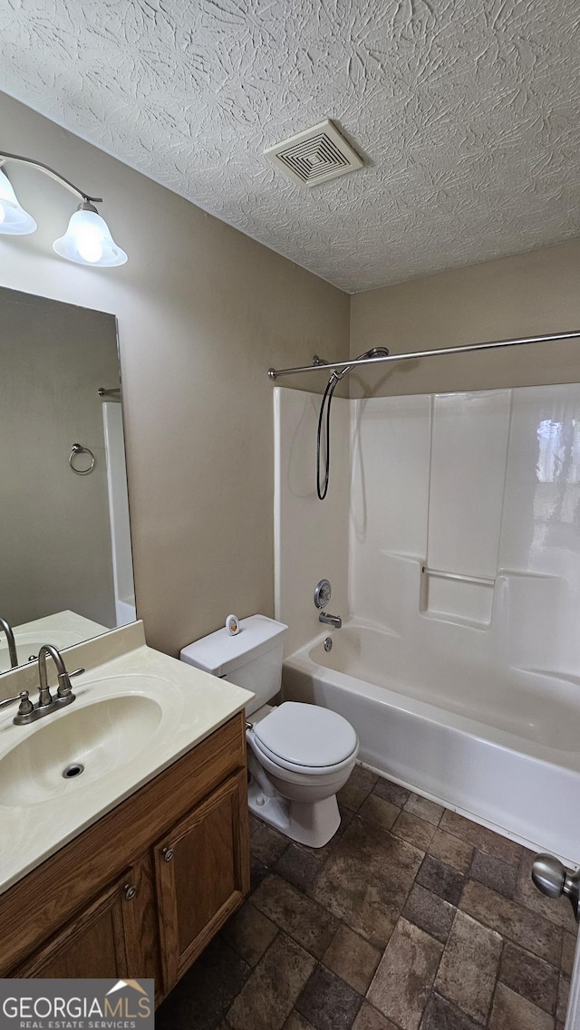 bathroom with shower / bath combination, toilet, vanity, a textured ceiling, and stone finish floors