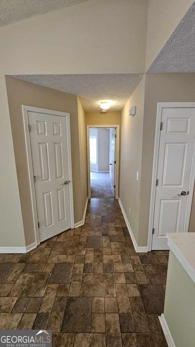 hall featuring stone tile flooring, a textured ceiling, and baseboards