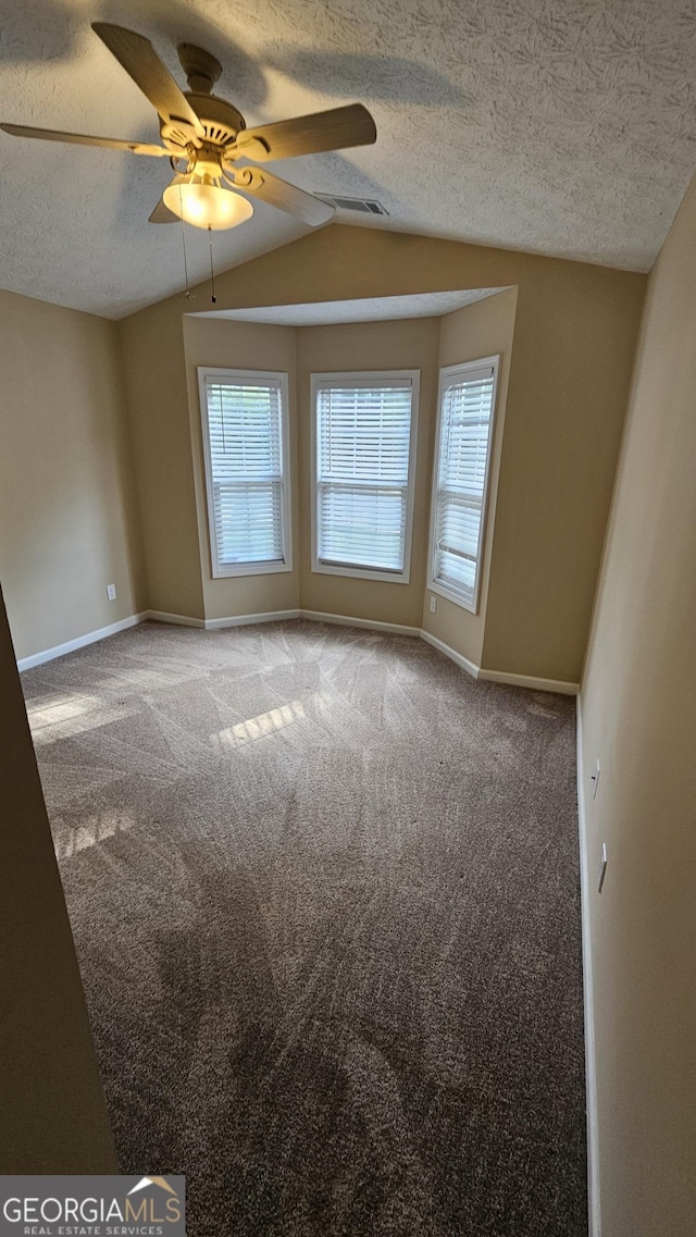 carpeted empty room with vaulted ceiling, baseboards, a textured ceiling, and a ceiling fan