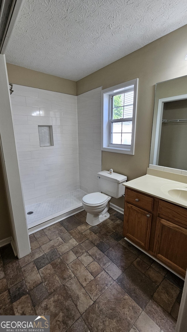 full bath with tiled shower, toilet, vanity, stone tile flooring, and a textured ceiling