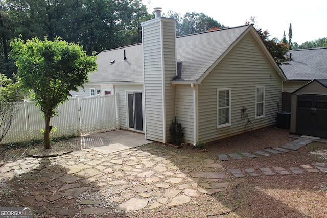 rear view of property featuring a patio, a storage shed, fence, an outbuilding, and a shingled roof