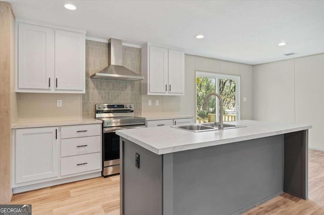kitchen with wall chimney range hood, electric range, a sink, light countertops, and white cabinetry