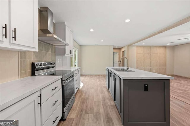 kitchen with stainless steel appliances, a sink, wall chimney range hood, light wood-type flooring, and a center island with sink