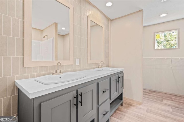 bathroom with tile walls, wood finished floors, double vanity, and recessed lighting