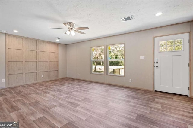unfurnished living room featuring ceiling fan, a decorative wall, light wood-style floors, recessed lighting, and a textured ceiling