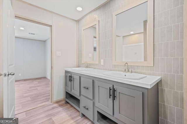 bathroom featuring tile walls, wood finished floors, double vanity, and decorative backsplash