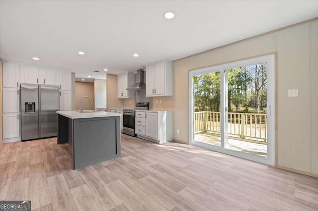 kitchen with stainless steel appliances, wall chimney range hood, a sink, light countertops, and light wood-style floors