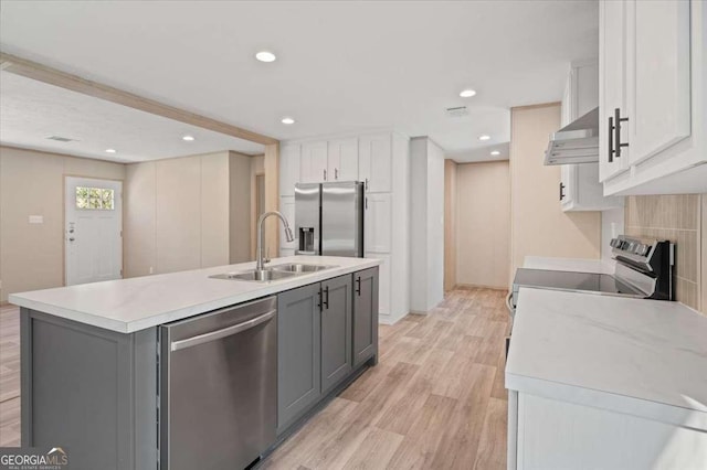 kitchen with stainless steel appliances, under cabinet range hood, a sink, light countertops, and light wood-type flooring