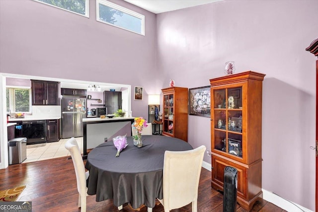 dining space with a high ceiling, light wood-style flooring, beverage cooler, and baseboards