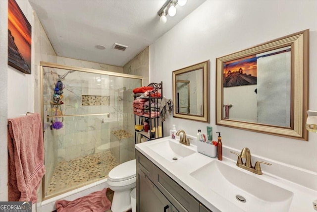 bathroom with a stall shower, toilet, and double vanity