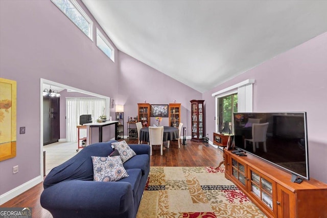 living room featuring high vaulted ceiling, wood finished floors, baseboards, and a chandelier