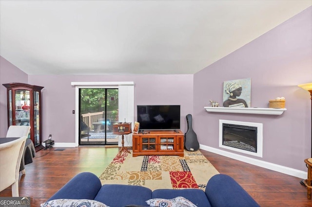 living room featuring vaulted ceiling, a glass covered fireplace, wood finished floors, and baseboards