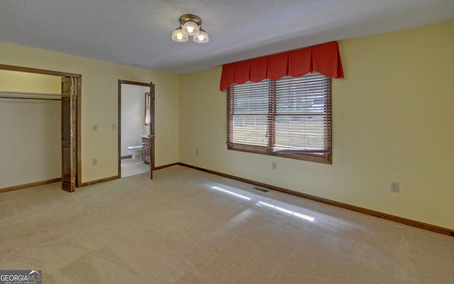 unfurnished bedroom featuring light colored carpet, ensuite bathroom, baseboards, and a closet