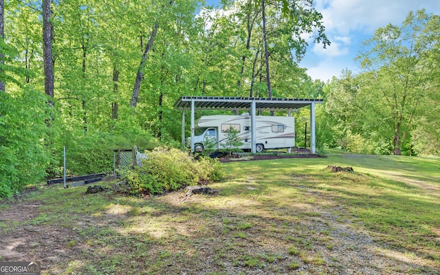 view of green lawn featuring a detached carport and a forest view